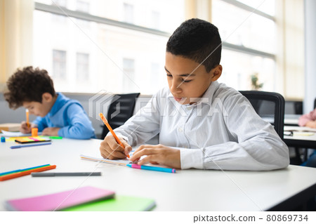 Portrait of small boy sitting at desk and writing Portrait of small boy sitting at desk and writing 80869734