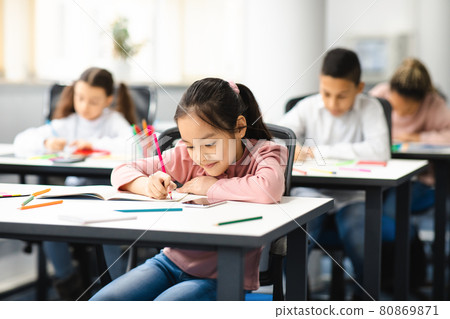 Portrait of diverse schoolchildren sitting in classroom writing and drawing 80869871