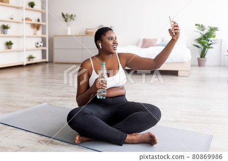 Plus size black woman taking selfie on break from home training, video chatting to personal coach on web at home 80869986