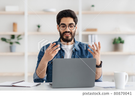 Online meeting. Happy young arab entrepreneur having video conference via laptop, talking and gesturing at camera Online meeting. Happy young arab entrepreneur having video conference via laptop, talking and gesturing at camera 80870041