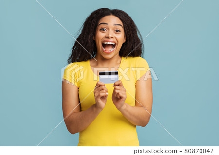 Trustful bank. Overjoyed african american woman demonstrating credit card and opening mouth in excitement Trustful bank. Overjoyed african american woman demonstrating credit card and opening mouth in excitement 80870042