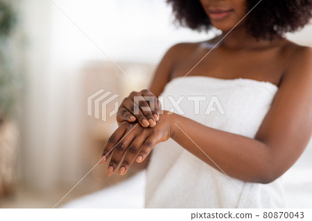 Unrecognizable young Afro lady applying hand cream after shower, wearing white towel indoors, copy space Unrecognizable young Afro lady applying hand cream after shower, wearing white towel indoors, copy space 80870043