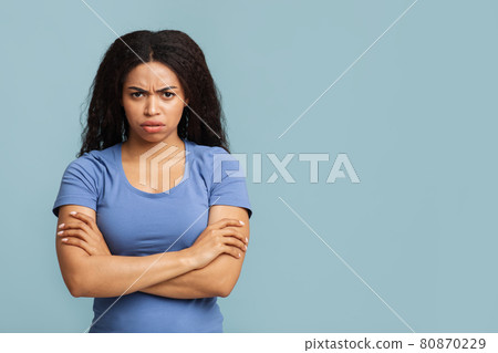 Grumpy woman. Portrait of serious black lady standing with crossed arms, posing over blue background with free space Grumpy woman. Portrait of serious black lady standing with crossed arms, posing over blue background with free space 80870229