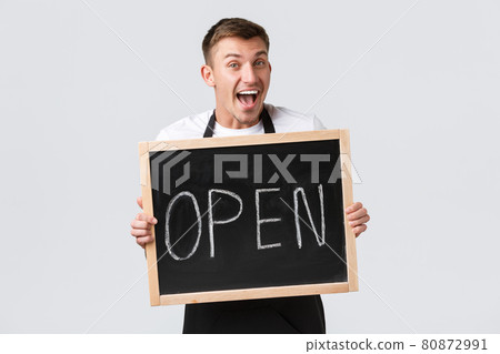 Small retail business owners, cafe and restaurant employees concept. Cheerful smiling barista greeting guests, salesman showing we are open sign and grinning upbeat, white background 80872991