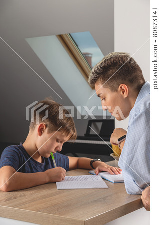 Kid boy doing homework at kitchen table with book 80873141