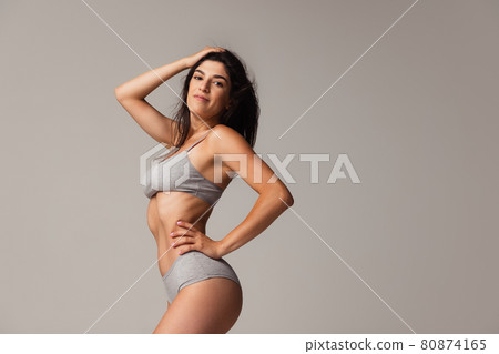 Portrait of young beautiful slim woman in lingerie posing isolated over gray studio background. Natural beauty concept. Portrait of young beautiful slim woman in lingerie posing isolated over gray studio background. Natural beauty concept. 80874165