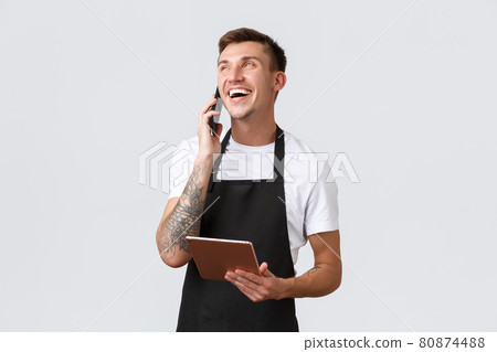 Retail stores, small business, cafe and restaurants takeaway concept. Handsome smiling salesman, barista talking on phone, laughing happy, taking order for delivery, holding digital tablet 80874488