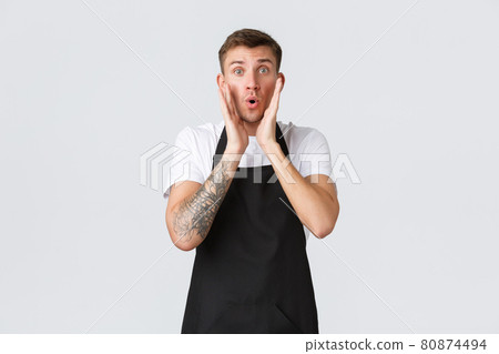 Small business owners, coffee shop and staff concept. Surprised blond guy barista, waiter in black apron, looking shocked and astounded by big news, cafe advertisement, white background 80874494