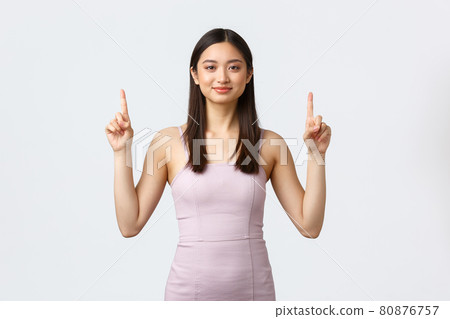 Luxury women, party and holidays concept. Happy young elegant woman in prom dress, pointing fingers up to show special offer at shop, smiling camera cheerful, white background Luxury women, party and holidays concept. Happy young elegant woman in prom dress, pointing fingers up to show special offer at shop, smiling camera cheerful, white background 80876757