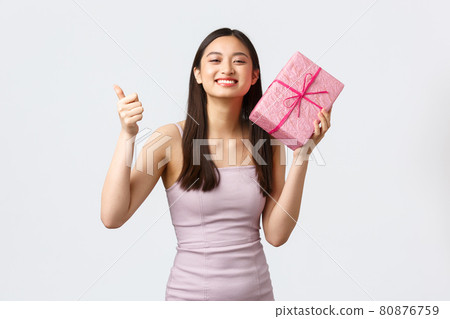 Celebration, party and holidays concept. Pleased happy beautiful birthday girl in evening dress, show thumbs-up and thanking for awesome gift, holding present box, white background Celebration, party and holidays concept. Pleased happy beautiful birthday girl in evening dress, show thumbs-up and thanking for awesome gift, holding present box, white background 80876759