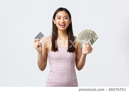 Luxury women, party and holidays concept. Cheerful elegant asian woman in dress, holding money and credit card with happy satisfied face, shopping over white background Luxury women, party and holidays concept. Cheerful elegant asian woman in dress, holding money and credit card with happy satisfied face, shopping over white background 80876761