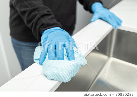 Hands in protective glove cleaning a modern sink with rag of a minimalist domestic kitchen Hands in protective glove cleaning a modern sink with rag of a minimalist domestic kitchen 80880282