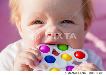 A smiling child in nature nibbles a bright colored toy with milk teeth A smiling child in nature nibbles a bright colored toy with milk teeth 80880305