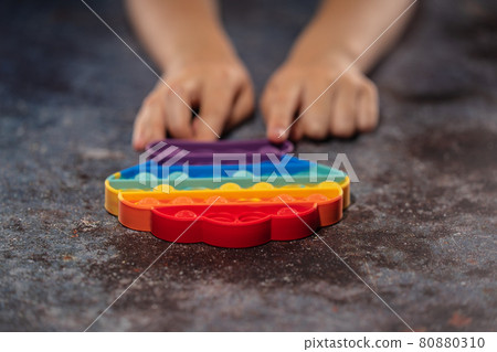 Little girl playing with rainbow colored pop it silicone toy antistress Little girl playing with rainbow colored pop it silicone toy antistress 80880310