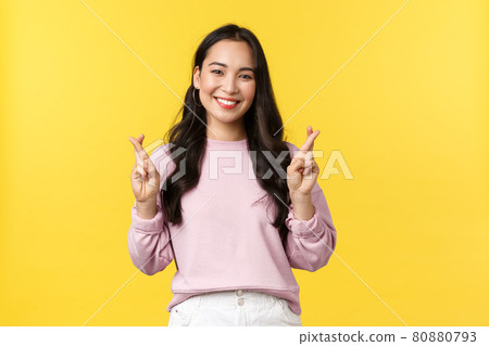 People emotions, lifestyle and fashion concept. Hopeful and optimistic cute asian girl having high hopes, cross fingers good luck and smiling, making wish, standing yellow background 80880793