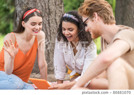 Three joyful young friends with tablet outdoors Three joyful young friends with tablet outdoors 80881070