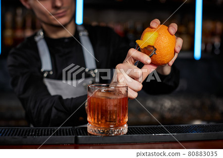 bartender makes a cocktail in a glass with orange peel 80883035