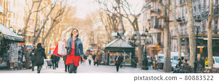 Happy Asian woman walking on La Rambla city street with shopping bags from open stores outside. Urban background panoramic. 80883522