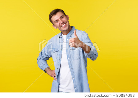 Portrait of satisfied proud young handsome man congratulate person for accomplishing goal, show thumbs-up delighted, smiling pleased. Man recommending awesome offer, stand yellow background 80884398