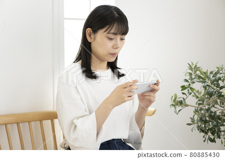 一位女士坐在房間的椅子上，操作智能手機 80885430