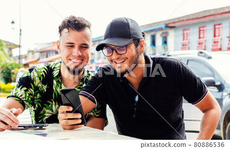 two young bearded latino men bonding in a public park looking at the smartphone. two young bearded latino men bonding in a public park looking at the smartphone. 80886536