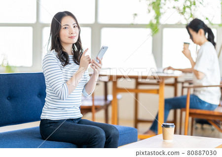 A young woman operating a smartphone in a coworking space. 80887030
