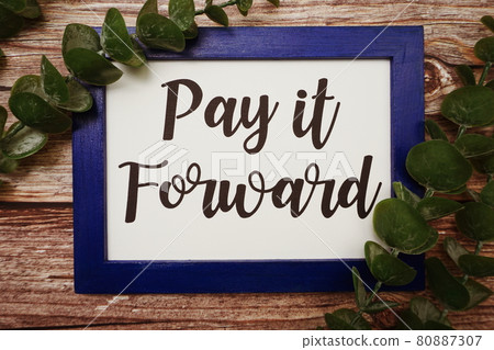 Pay it Forward written on blue frame with green leave flat lay on wooden background Pay it Forward written on blue frame with green leave flat lay on wooden background 80887307