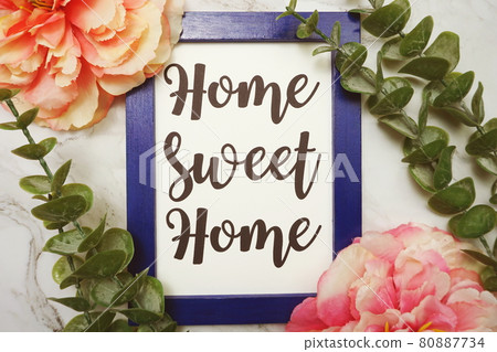 Home Sweet Home written on blue frame with green leave and pink flower flat lay on marble background 80887734