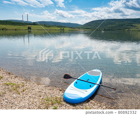 Abandoned modern stand up paddleboard by gravel shore. Abandoned modern stand up paddleboard by gravel shore. 80892332