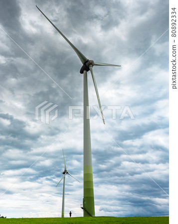 Contrast giant wind turbines and a boy at the foot of a pole. Contrast giant wind turbines and a boy at the foot of a pole. 80892334