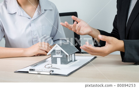 A real estate agent with a home model is talking to clients about renting a home and buying home insurance. Home rental and insurance concept 80894253