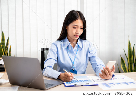 Asian women sit at their desks and calculate financial graphs showing results about their investments, plan a successful business growth process Asian women sit at their desks and calculate financial graphs showing results about their investments, plan a successful business growth process 80894302
