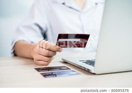 The businesswoman's hand is holding a credit card and using a laptop for online shopping and internet payment in the office 80895876
