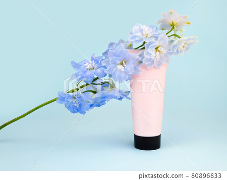 Unbranded pink squeeze bottle cream tube with black screw cap and blue Delphinium flower on blue background. Skincare beauty, mockup. Cosmetic bottle blank for branding and label, front view, closeup. 80896833