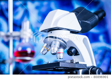 Close up shot of microscope in laboratory with beaker and red liquit blur in background. Close up shot of microscope in laboratory with beaker and red liquit blur in background. 80896901