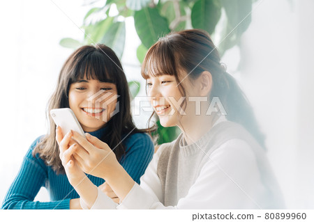 Two smiling women looking at a smartphone at a cafe 80899960
