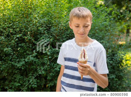 Teenager boy eating ice-cream cone on green nature background. Summer, junk food and people concept. Copyspace 80900398