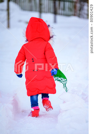 A happy girl in a red jacket and Ukrainian national kerchief walks in a snowy yard. 80901429