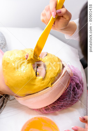 spa treatments in a beauty salon, hand of a professional beautician applying a gold mask on the client's face. spa treatments in a beauty salon, hand of a professional beautician applying a gold mask on the client's face. 80901438