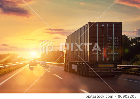Scenic front view big long heavy semi-treailer truck with sea shipping container driving highway dramatic warm morning evening sunrise sun sky sunset. Cargo transport industry background concept 80902205