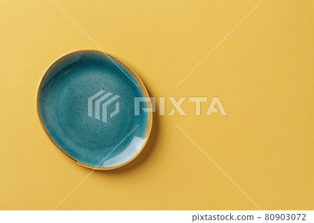 Turquoise teal oval ceramic plate over textured yellow background with copy space. 80903072
