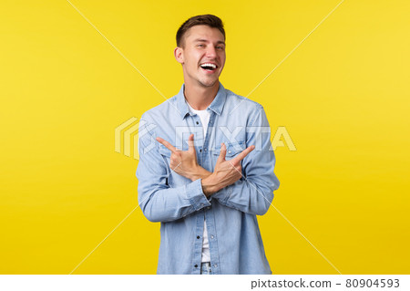 Portrait of charismatic handsome blond man laughing happy and pointing fingers sideways, showing left and right variants or products, standing cheerful over yellow background Portrait of charismatic handsome blond man laughing happy and pointing fingers sideways, showing left and right variants or products, standing cheerful over yellow background 80904593
