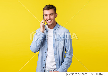 Technology, lifestyle and advertisement concept. Handsome modern young man in casual clothes, calling friend, talking on mobile phone and smiling at camera, standing yellow background Technology, lifestyle and advertisement concept. Handsome modern young man in casual clothes, calling friend, talking on mobile phone and smiling at camera, standing yellow background 80904628