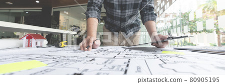 A male architect measuring and marking the scale ratio of sizes of a complicated blueprint 80905195