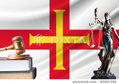 Law and justice in Guernsey. Statue of themis and the gavel of the judge against the background of the flag of Guernsey. Law and justice concept 80905399