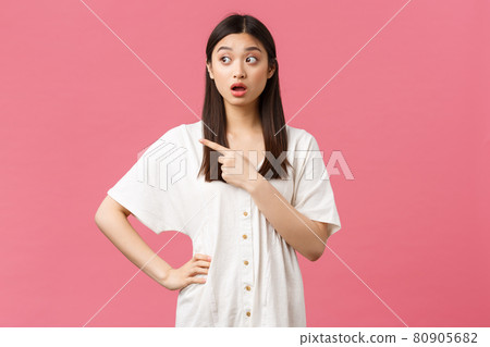 Beauty, people emotions and summer leisure and vacation concept. Confused asian girl looking puzzled and unsure, pointing finger looking left with intrigued surprised face, pink background 80905682