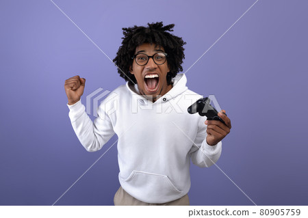 Triumphant black teen guy with joystick shouting in excitement, playing video game, making YES gesture 80905759