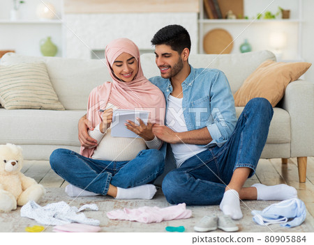 Preparing for childbirth. Pregnant muslim couple making checklist of baby things before going to maternity hospital 80905884