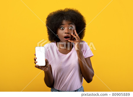 Shocking mobile news concept. Emotional black lady showing smartphone with blank screen over yellow background Shocking mobile news concept. Emotional black lady showing smartphone with blank screen over yellow background 80905889