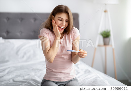Excited young woman checking her recent pregnancy test, feeling happy over future maternity on bed at home Excited young woman checking her recent pregnancy test, feeling happy over future maternity on bed at home 80906011